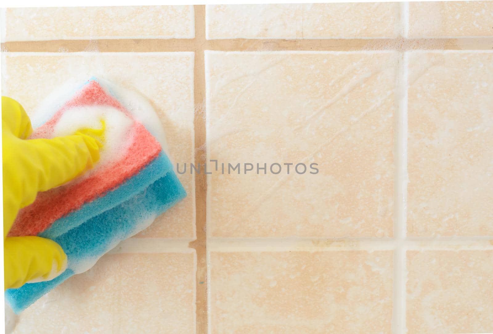 Hand in yellow protective glove washes tile with foam on ceramic tile background.Home cleaning. by andre_dechapelle