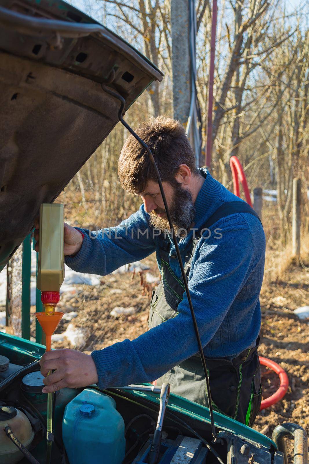 A man pours lubricating oil into the car. In the summer on the street next to the house.