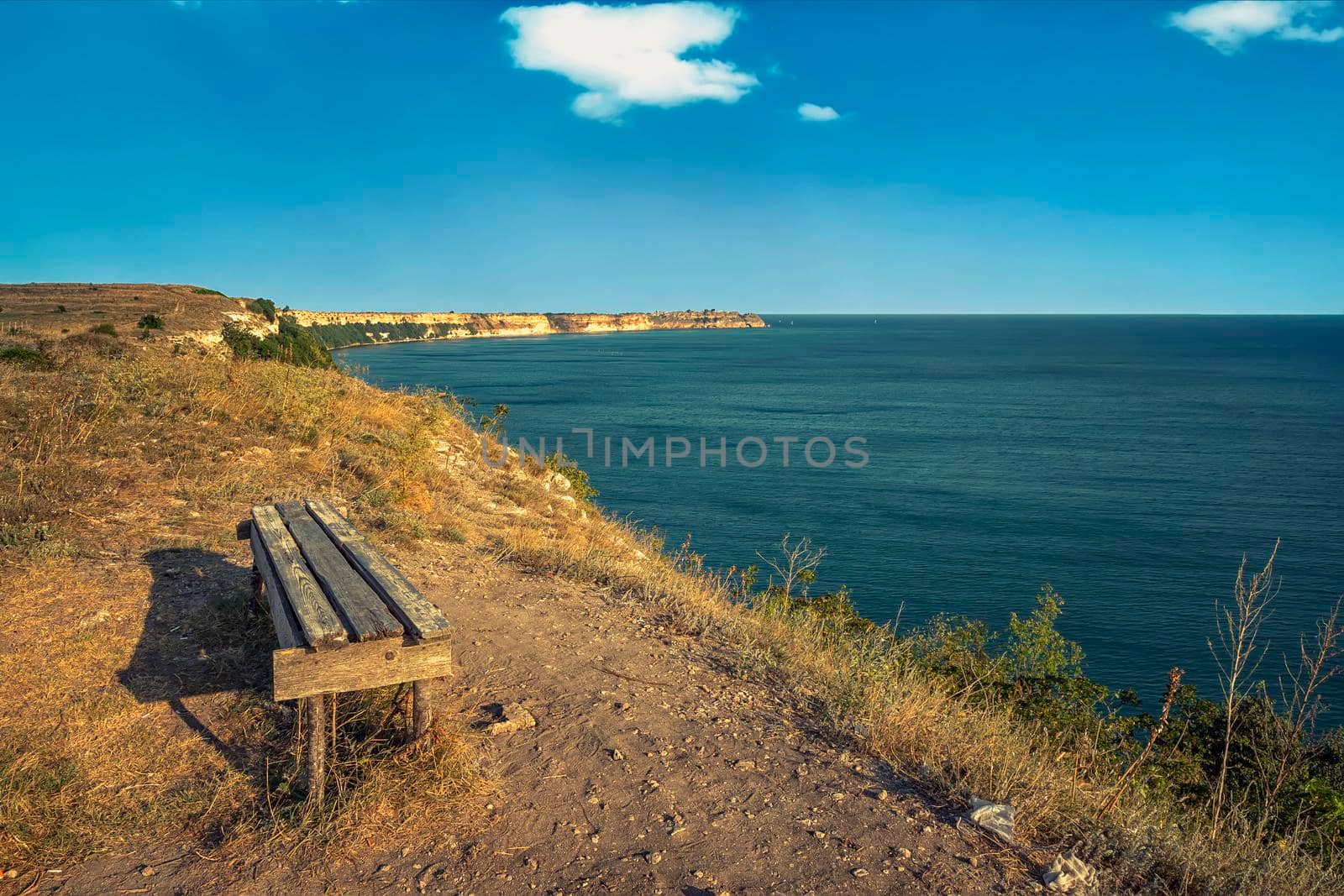 empty bench on the top of sea rocks with a vast view for relaxation by EdVal