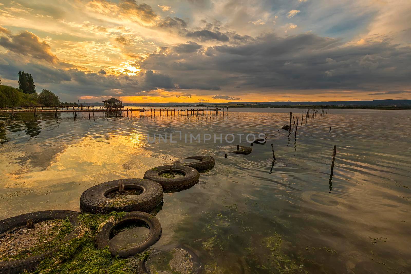 Beautiful sunset on the lake with fishing net in water and old tires  by EdVal