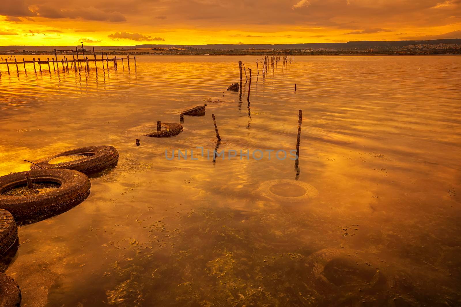 Colorful sunset on the lake with fishing net in water and old tires  by EdVal
