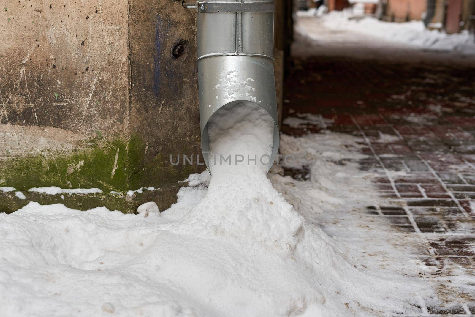 The metal drainpipe on the corner of the house is filled with snow. Close-up