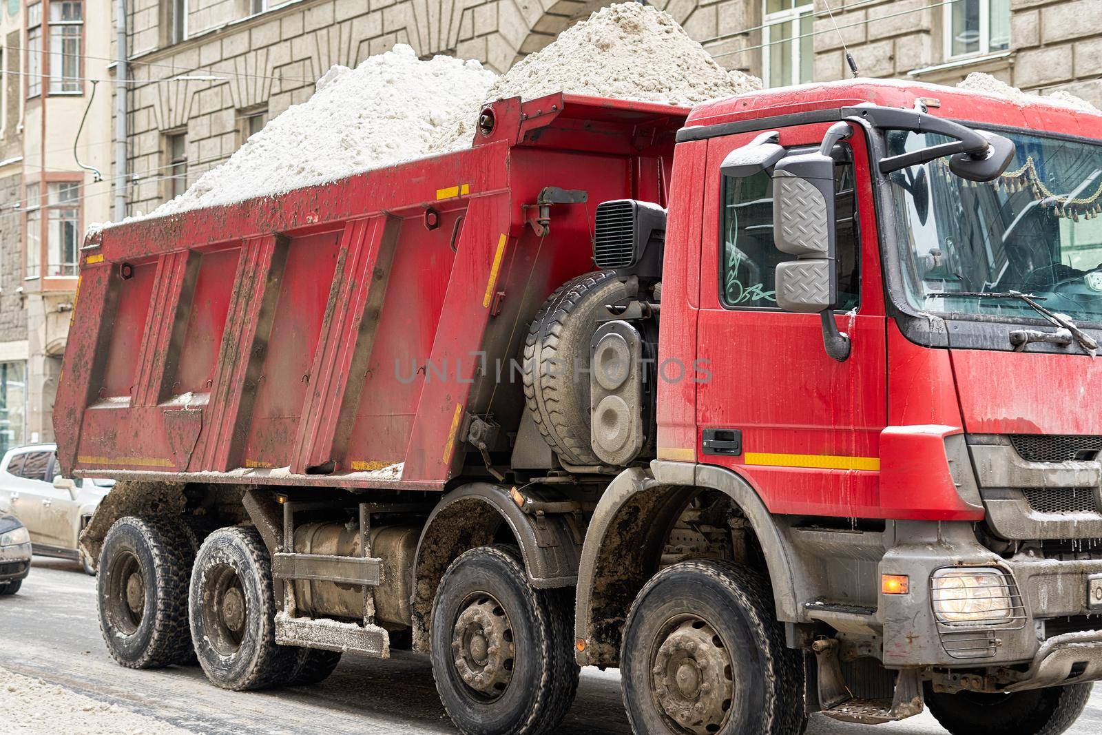 Dump truck loaded with snow driving through city street. Close up