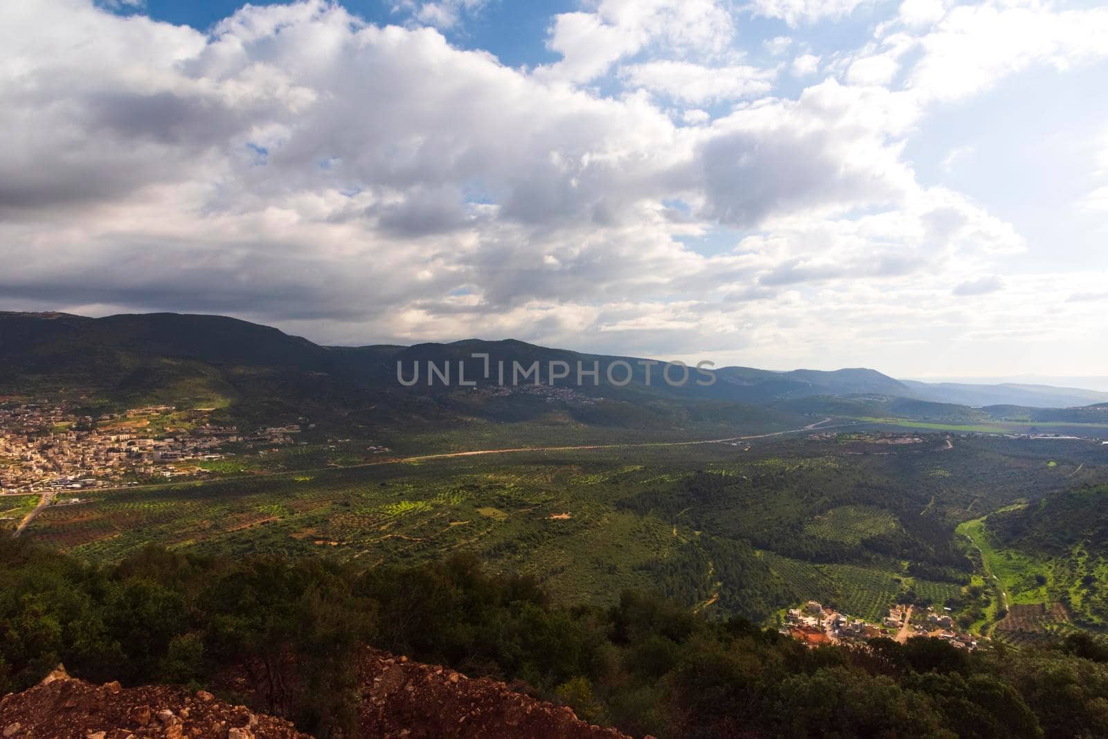 A view of a mountain range and a green valley in the morning at sunrise, against a dramatic back of blue skies and clouds. High quality photo. Travel concept hiking. North District Israel by avirozen