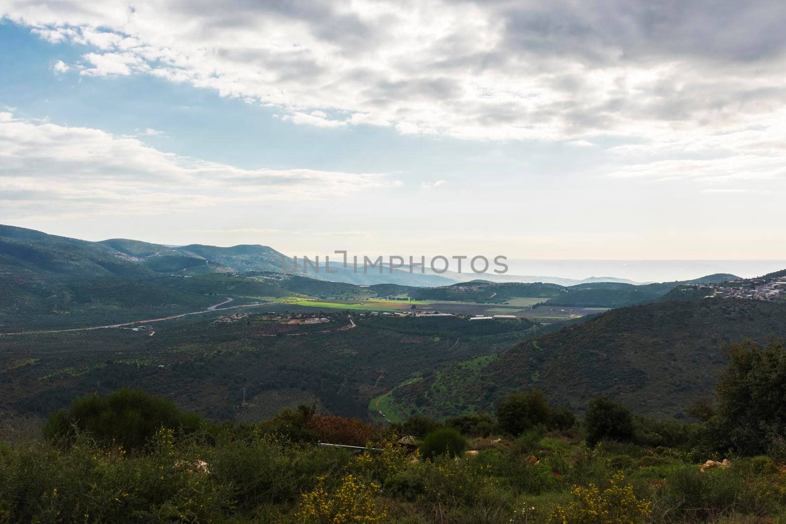 A view of a mountain range and a green valley in the morning at sunrise, against a dramatic backdrop of blue skies and clouds. North District Israel. High quality photo. Travel concept hiking