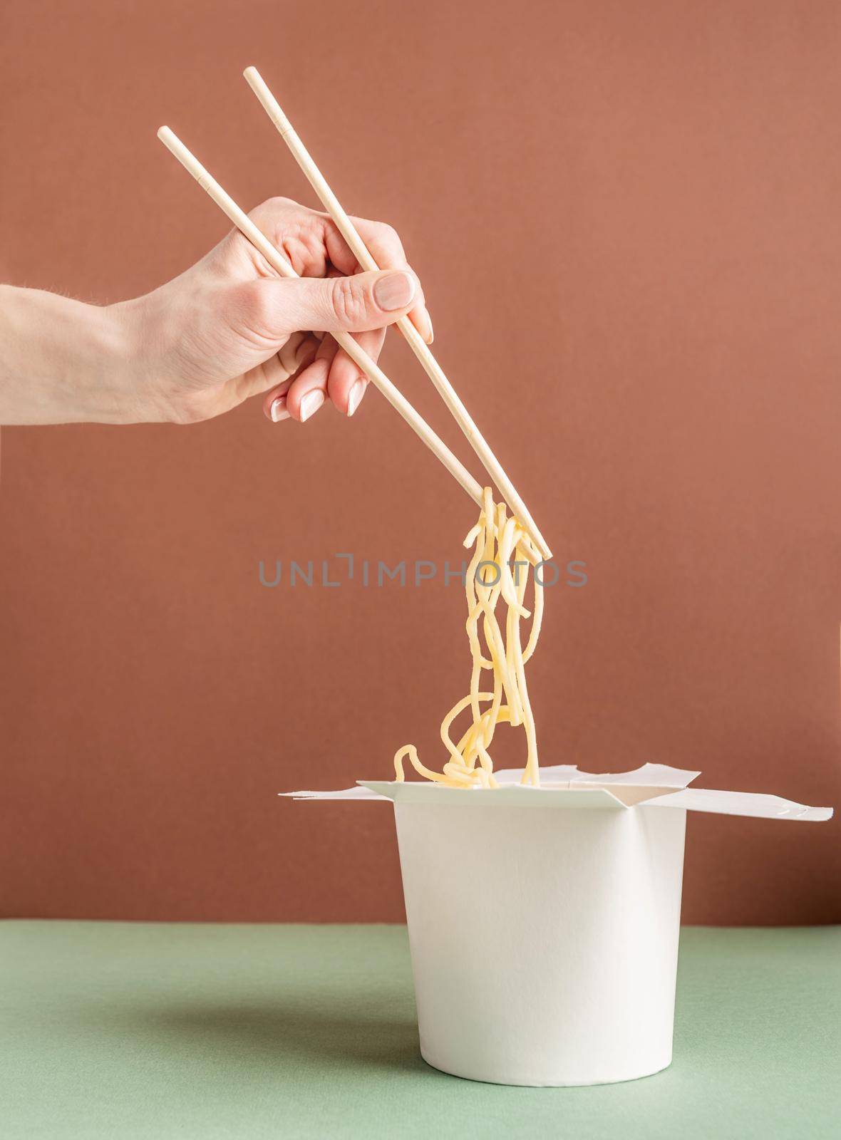 Zero waste and ecology concept. Opened WOK paper box for mock up design. Woman hand holding noodles with chopsticks