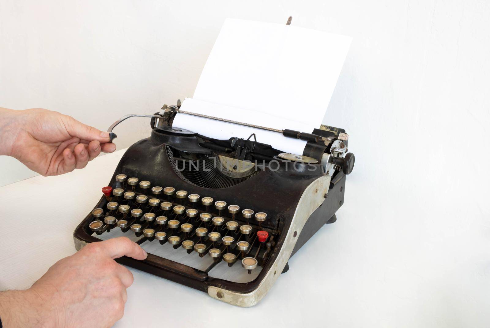 An old typewriter and a blank sheet of paper inserted. Isolated on a white background. The hands of the master set up the typewriter.