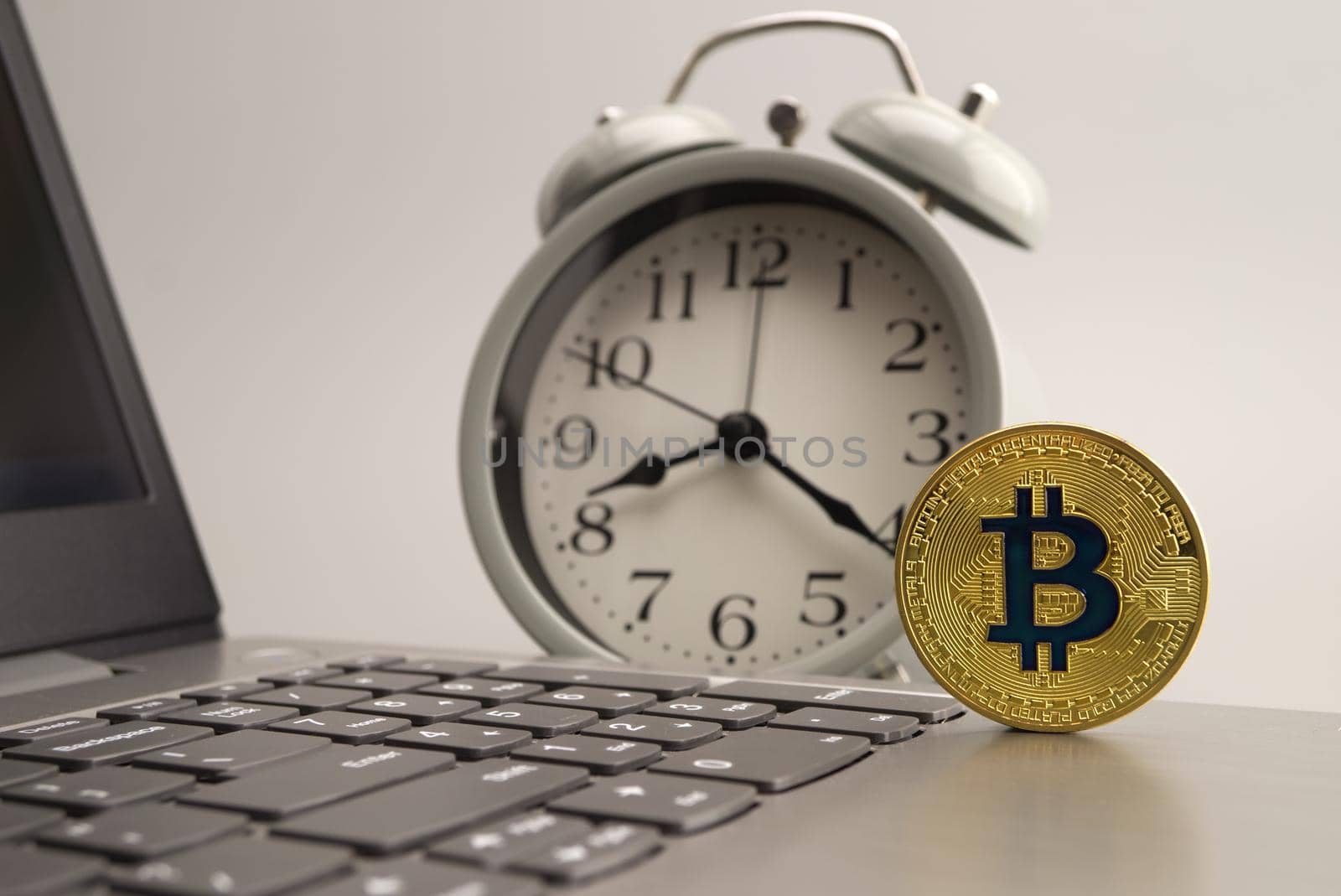 Golden Bitcoin on the computer keyboard next to the alarm clock. Digital or virtual currency concept, selective focus