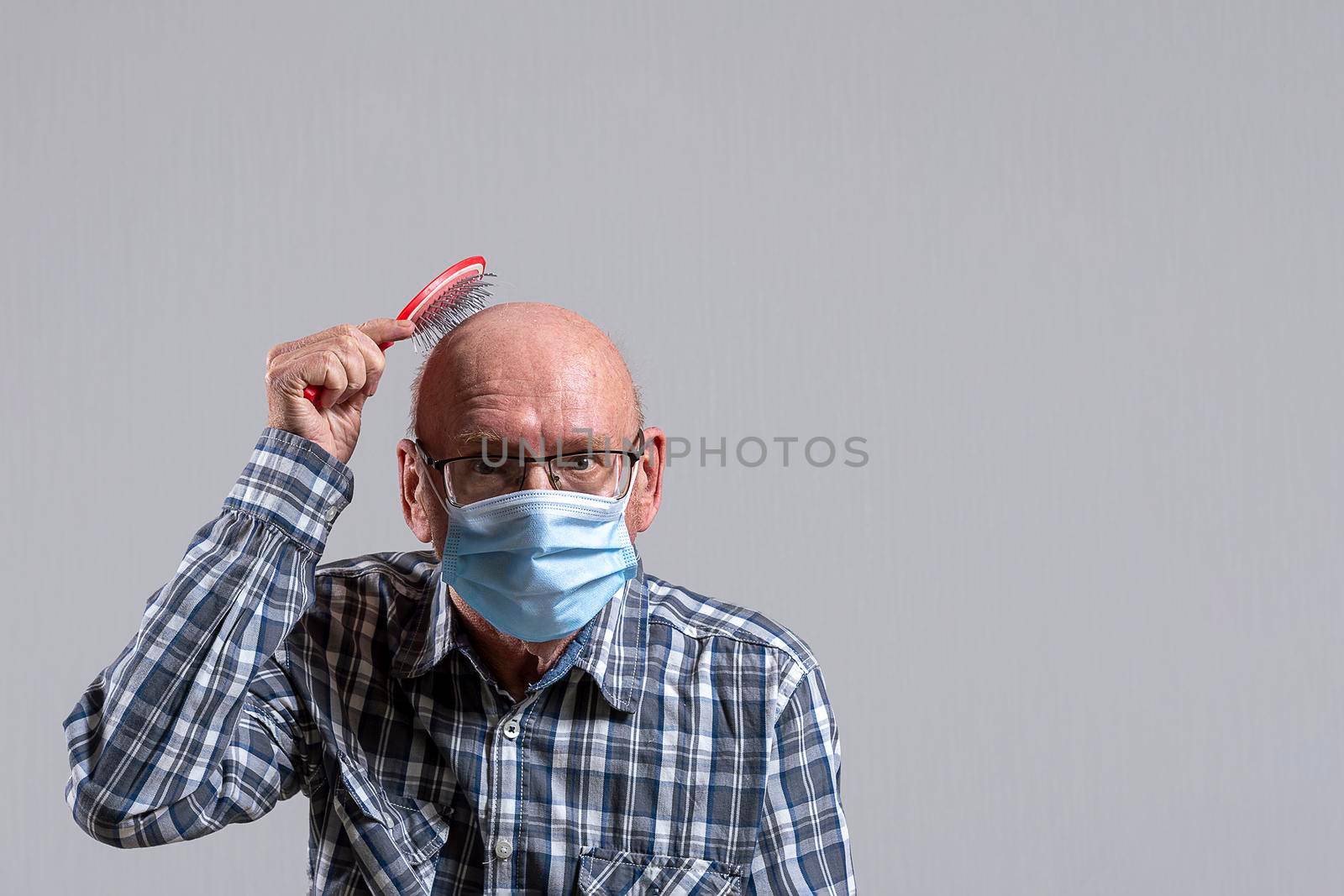 Old bald man with glasses and medical mask with hairbrush in his hand. Copy space. by Essffes