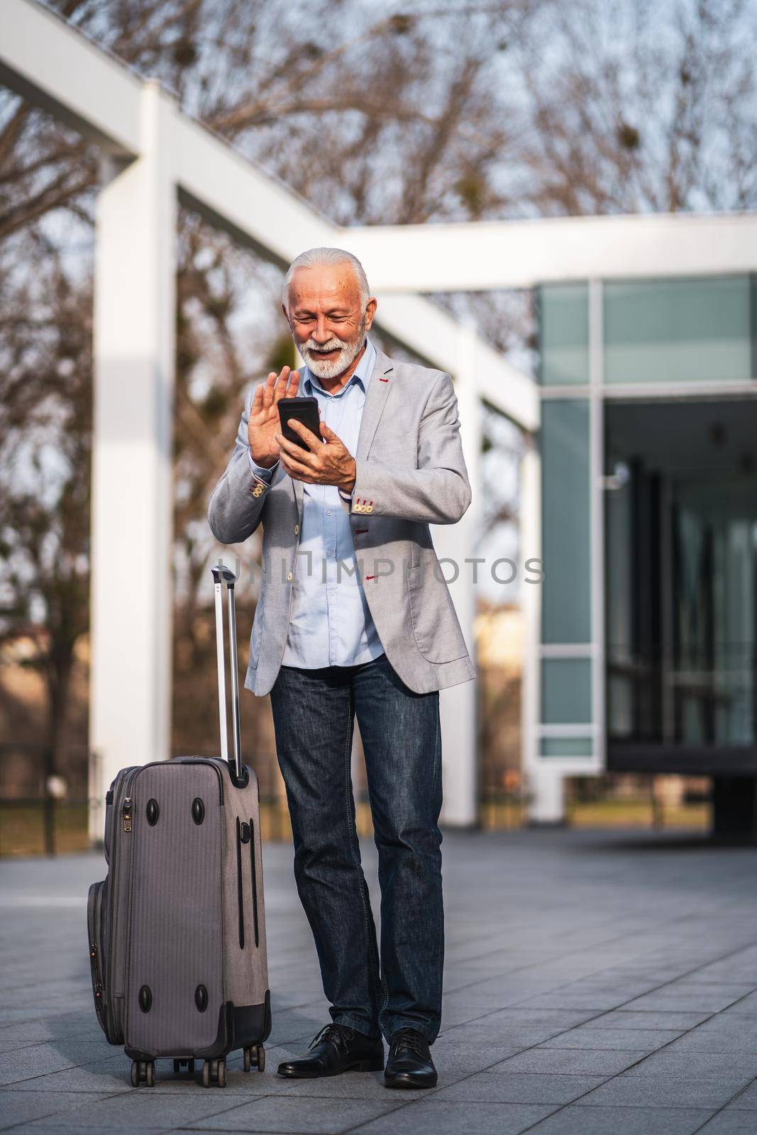 Happy senior businessman is arriving from business trip. He is messaging on smartphone.