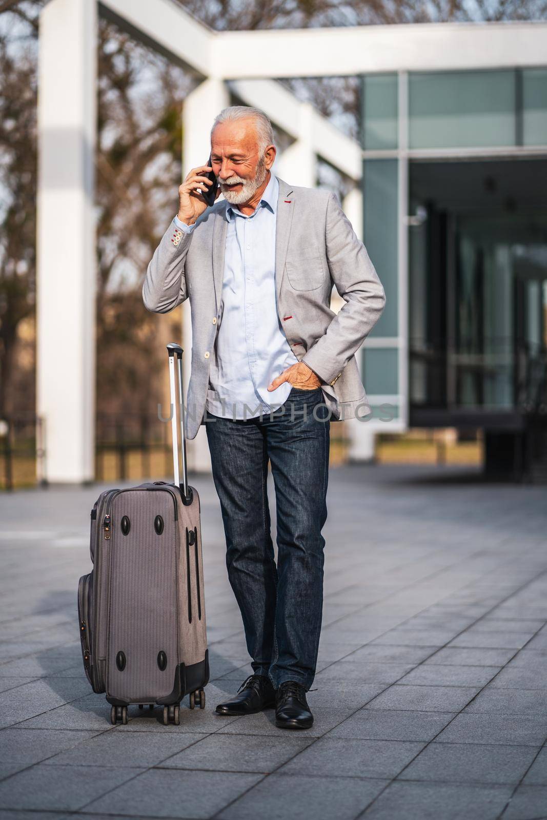 Happy senior businessman is arriving from business trip. He is talking on phone.
