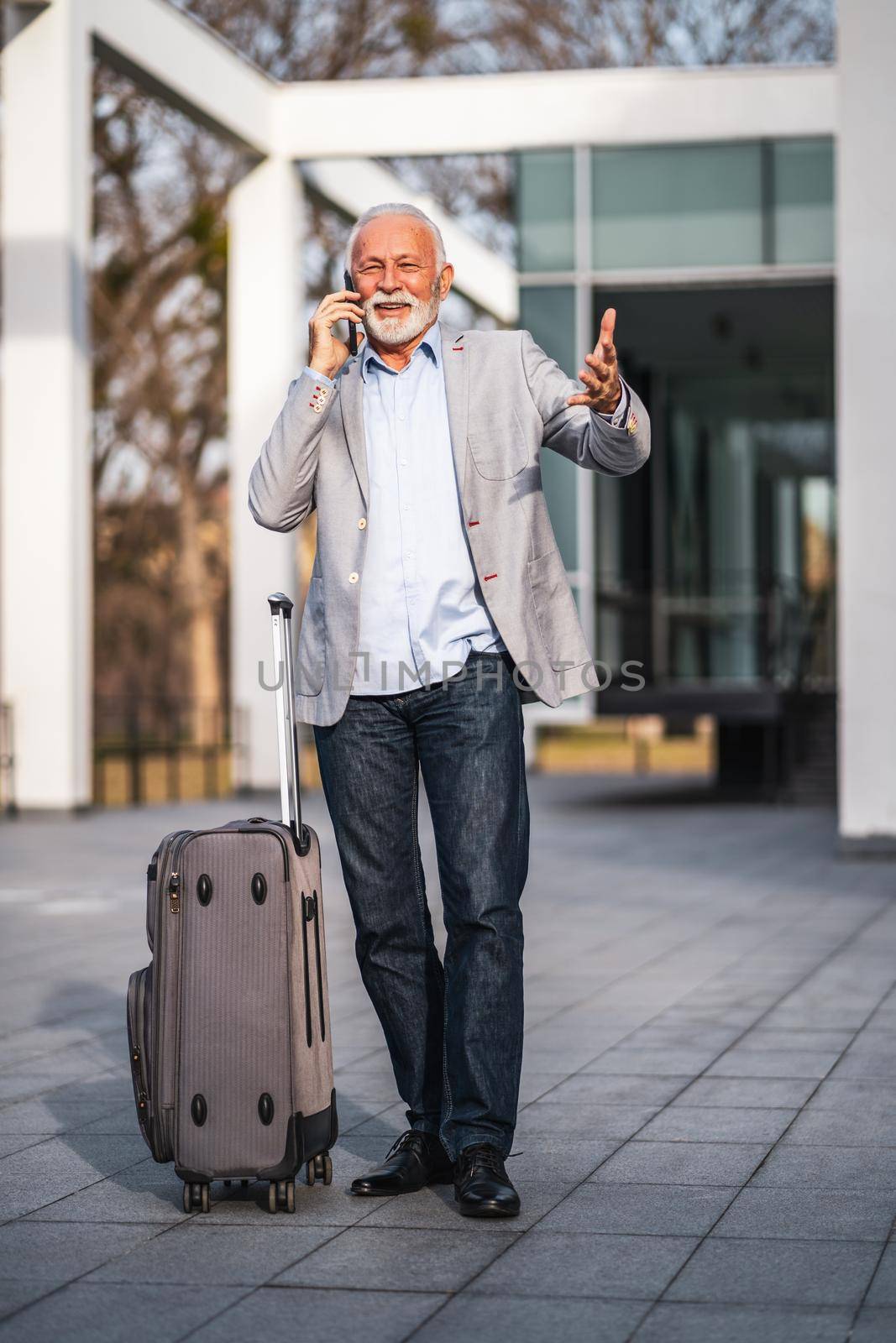 Happy senior businessman is arriving from business trip. He is talking on phone.