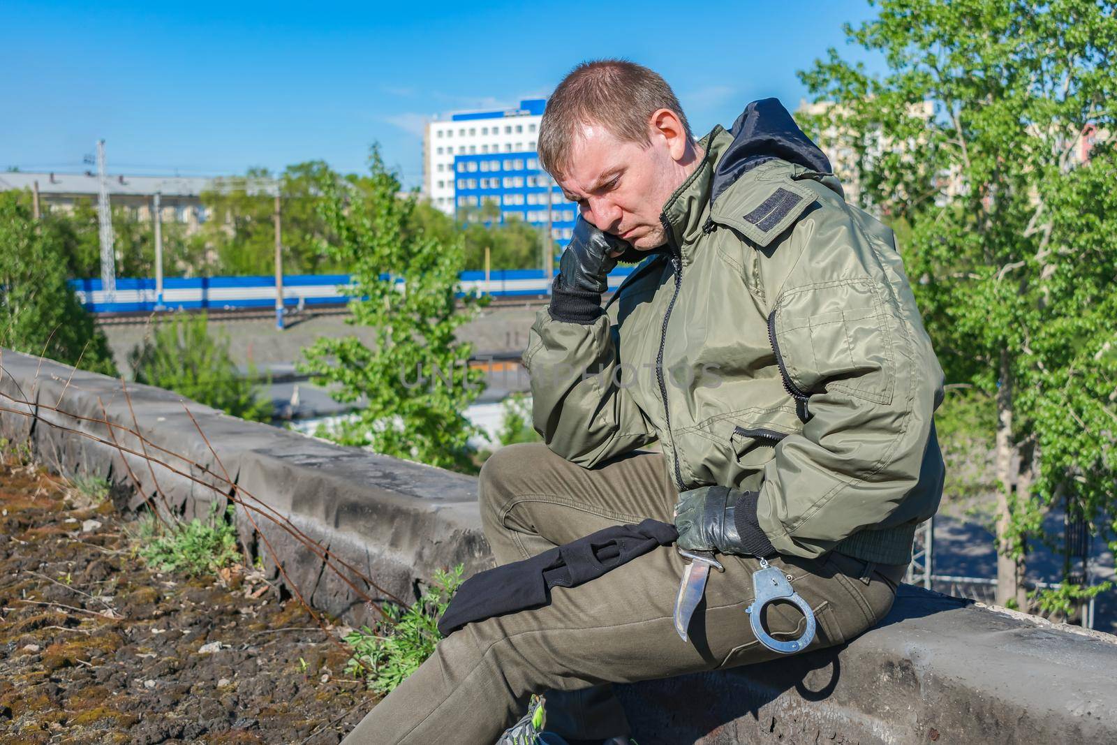 A pensive soldier sits quietly all alone on the street against the background of the city