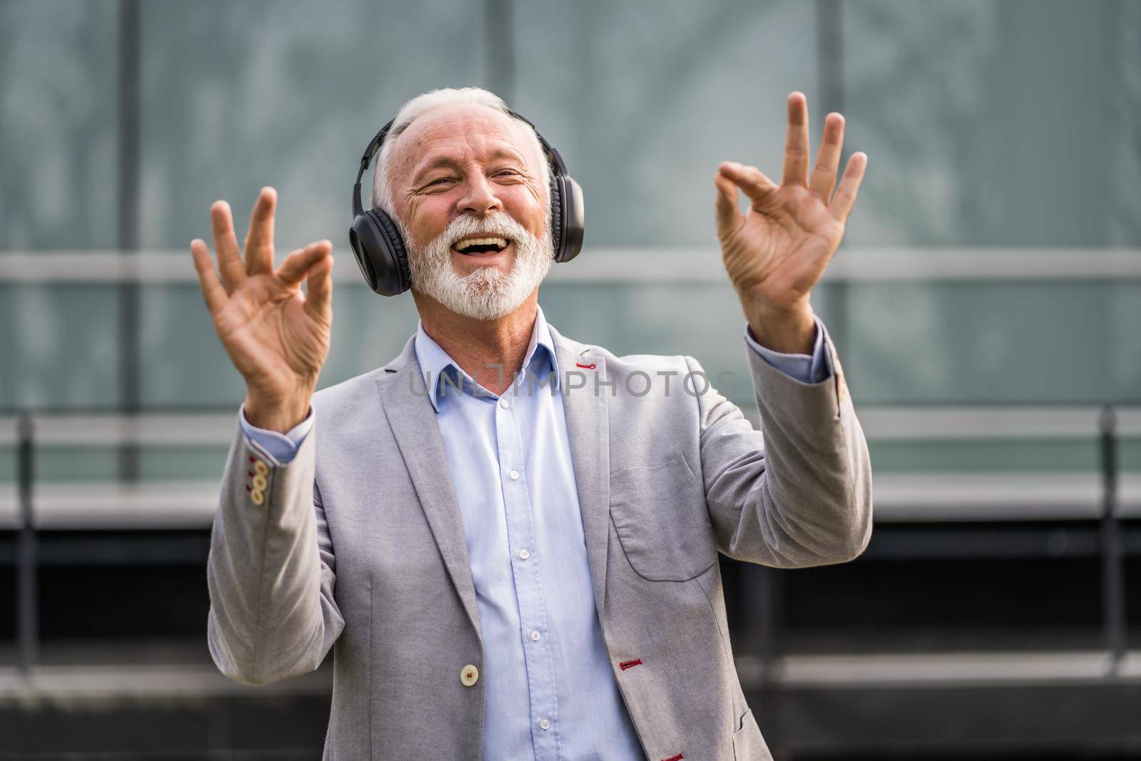 Outdoor portrait of senior businessman who is enjoying music on headphones.