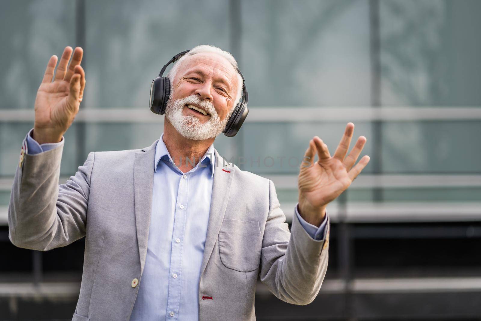 Outdoor portrait of senior businessman who is enjoying music on headphones.