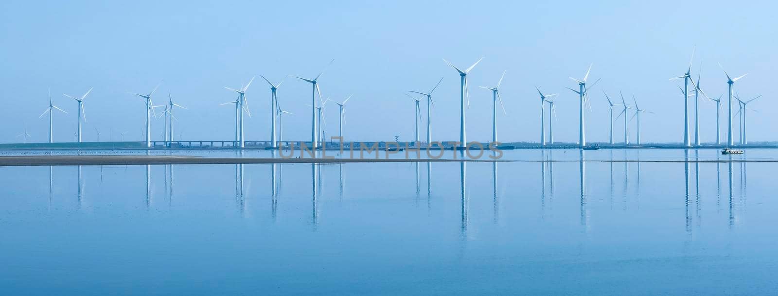 wind turbines reflected in water near philipsdam in dutch province of zeeland under blue sky