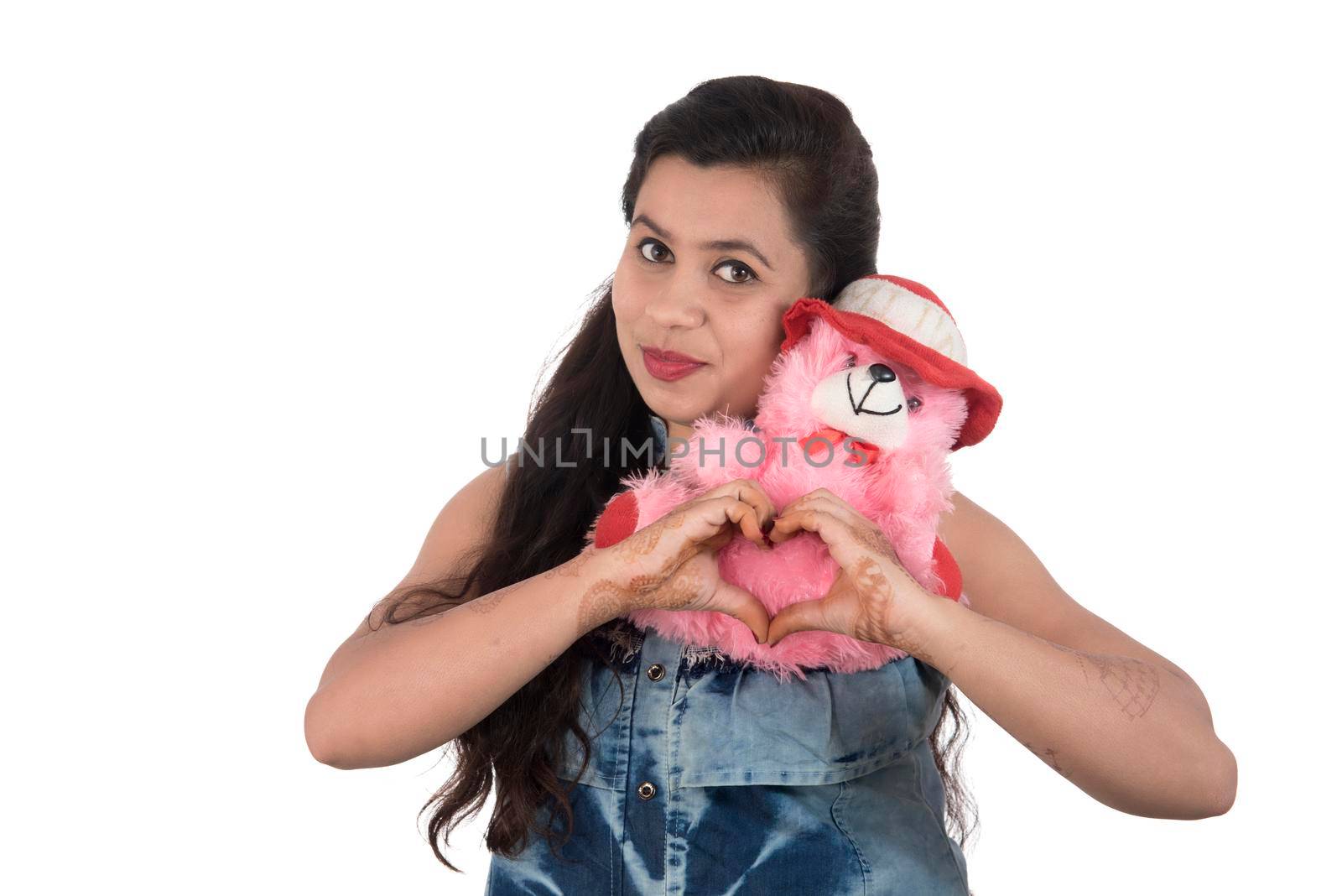 Beautiful young girl holding and playing with a teddy bear toy on a white background.