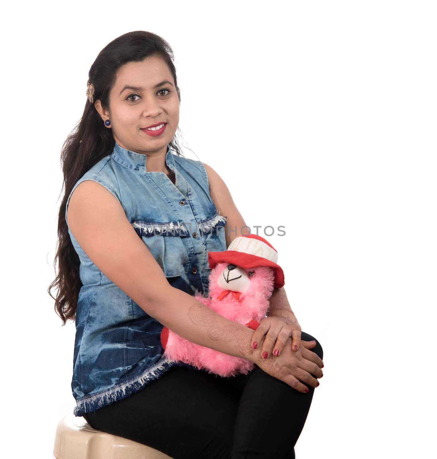 Beautiful young girl holding and playing with a teddy bear toy on a white background.