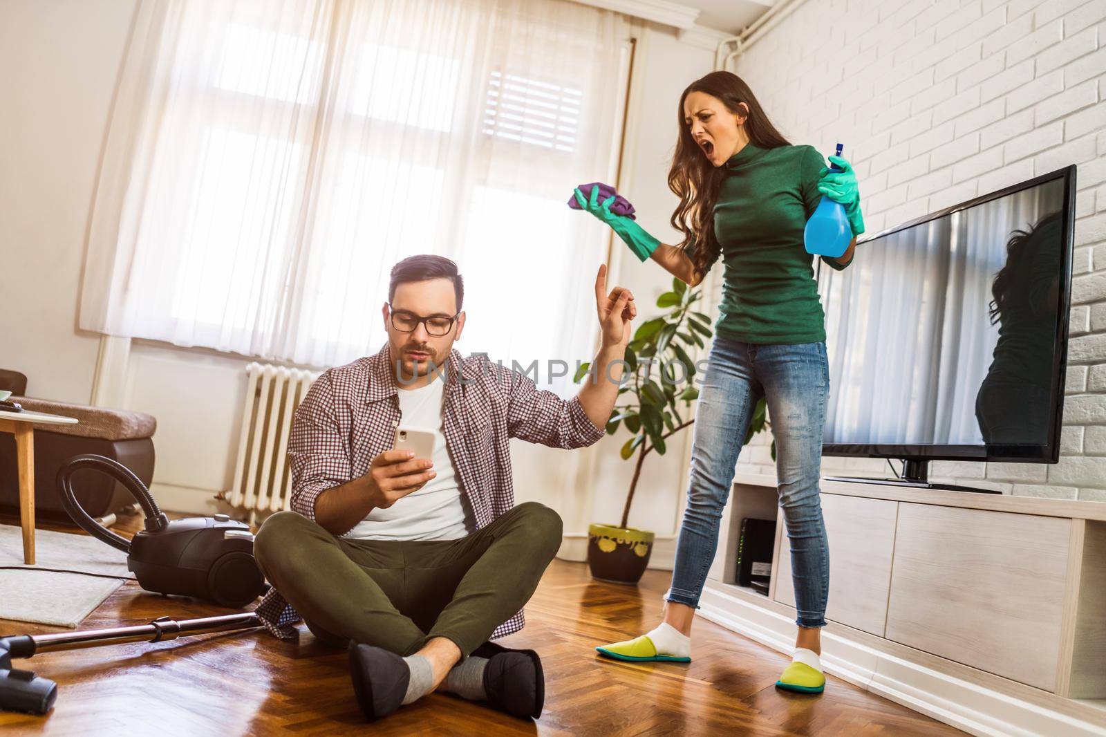 Man is lazy. His wife is telling him to continue cleaning their apartment.