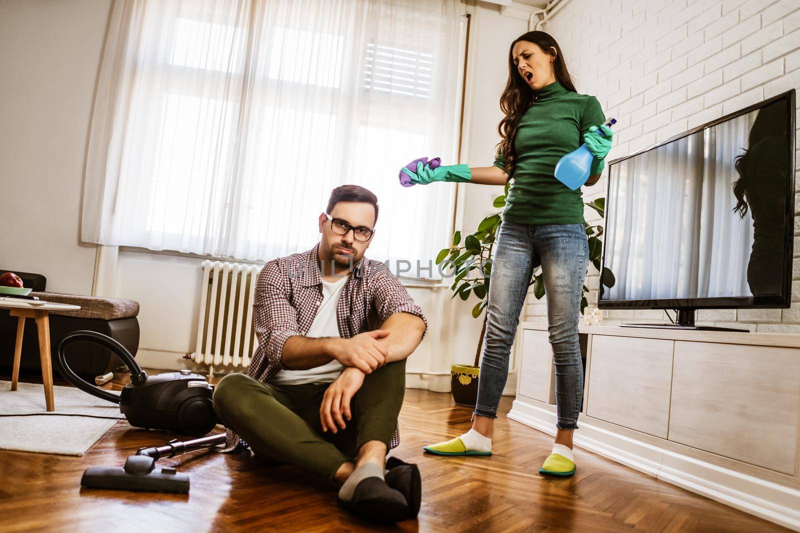 Man is lazy. His wife is telling him to continue cleaning their apartment.