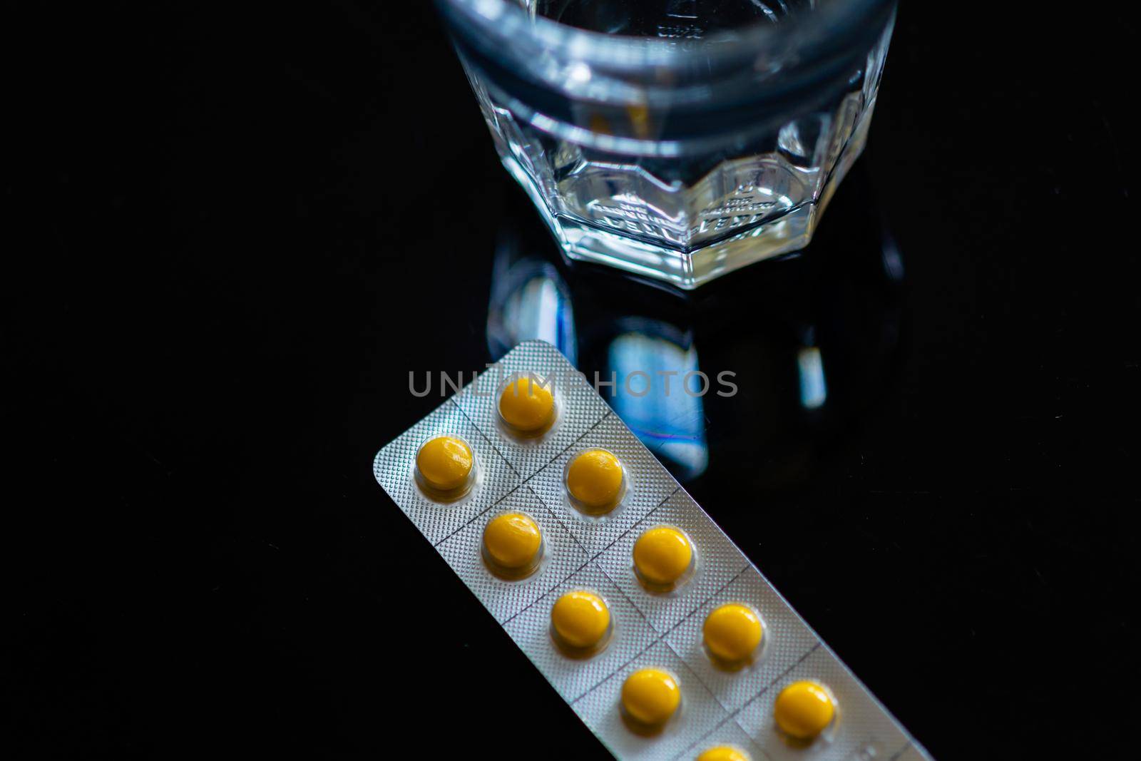 Yellow tablets in blister pack next to glass of water  on black background