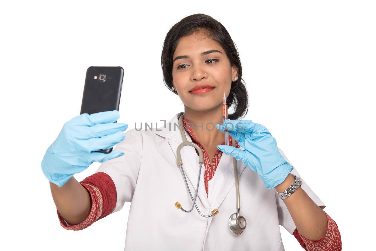 Female doctor taking selfie with stethoscope and injection by smartphone on white background. by DipakShelare