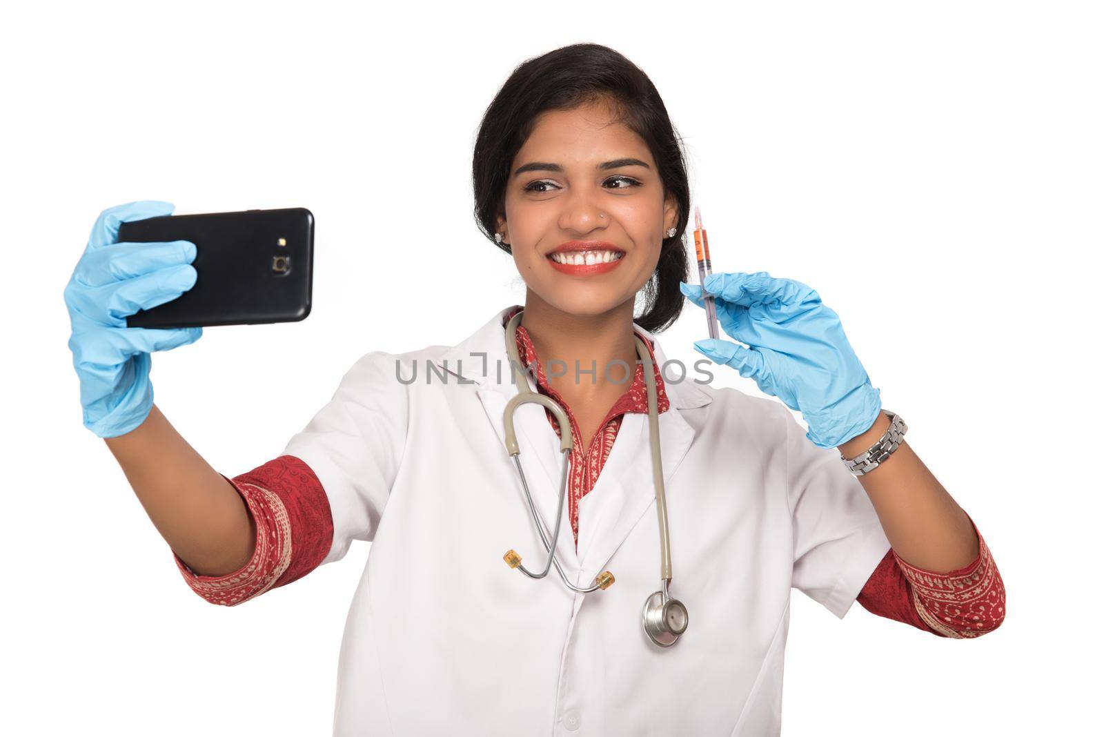 Female doctor taking selfie with stethoscope and injection by smartphone on white background.