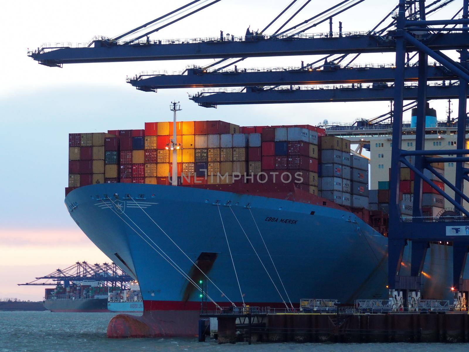 Port of Felixstowe, Suffolk, UK, February 11 2018: Cranes loading containers onto the Ebba Maersk cargo ship at dusk with sunset in background