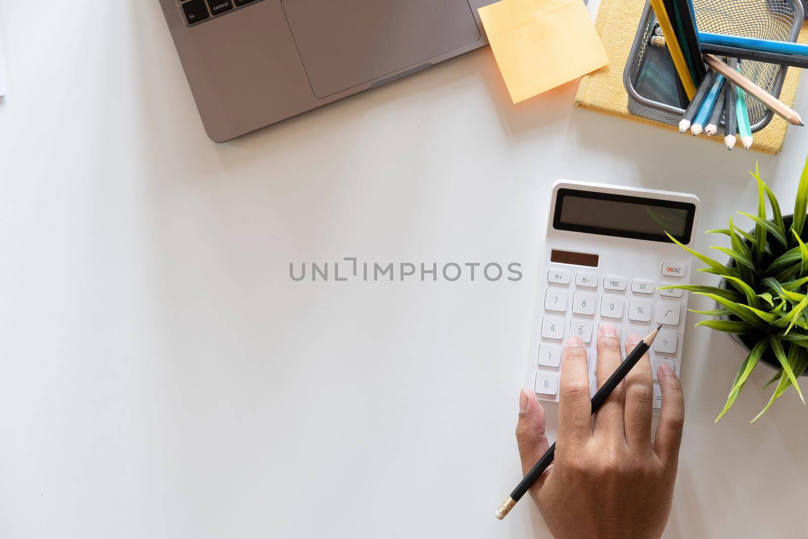 Top view hand of accountant using calculator on workplace with copy space, calculator and plant potted on white desk background, Accounting workplace concept by nateemee
