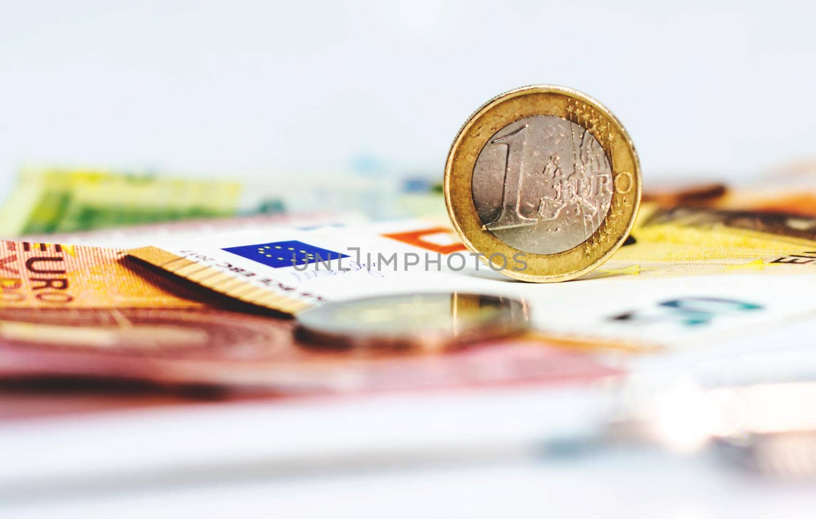 A used 1 euro coin standing on top of some euro banknotes by rarrarorro