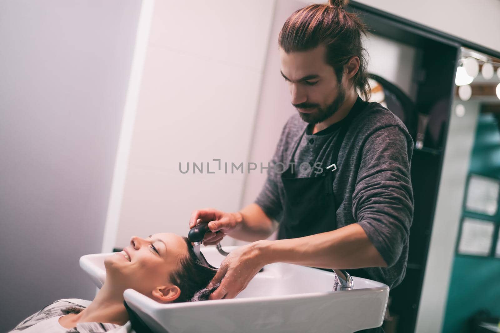 Young woman getting new hairstyle at professional hair styling saloon. Hairdresser is washing and massaging her head.