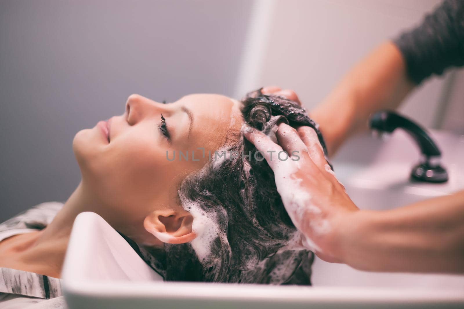 Young woman getting new hairstyle at professional hair styling saloon. Hairdresser is washing and massaging her head.