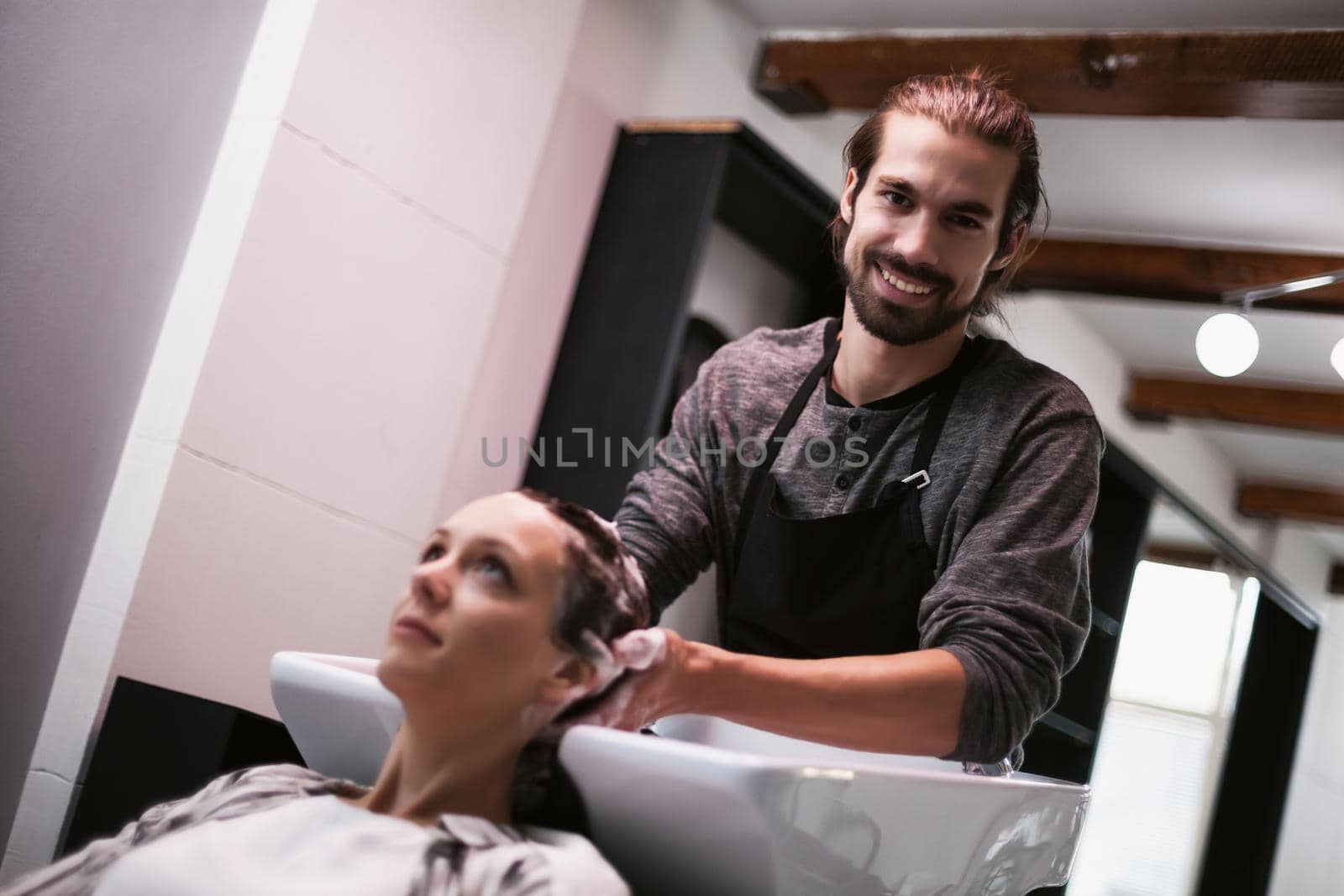 Young woman getting new hairstyle at professional hair styling saloon. Hairdresser is washing and massaging her head.