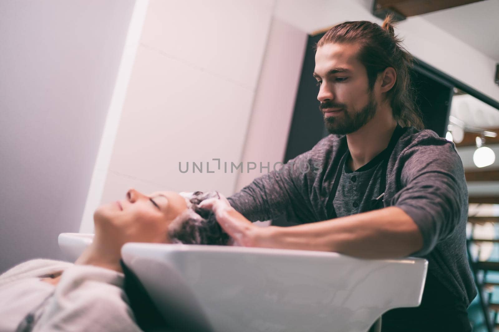 Young woman getting new hairstyle at professional hair styling saloon. Hairdresser is washing and massaging her head.