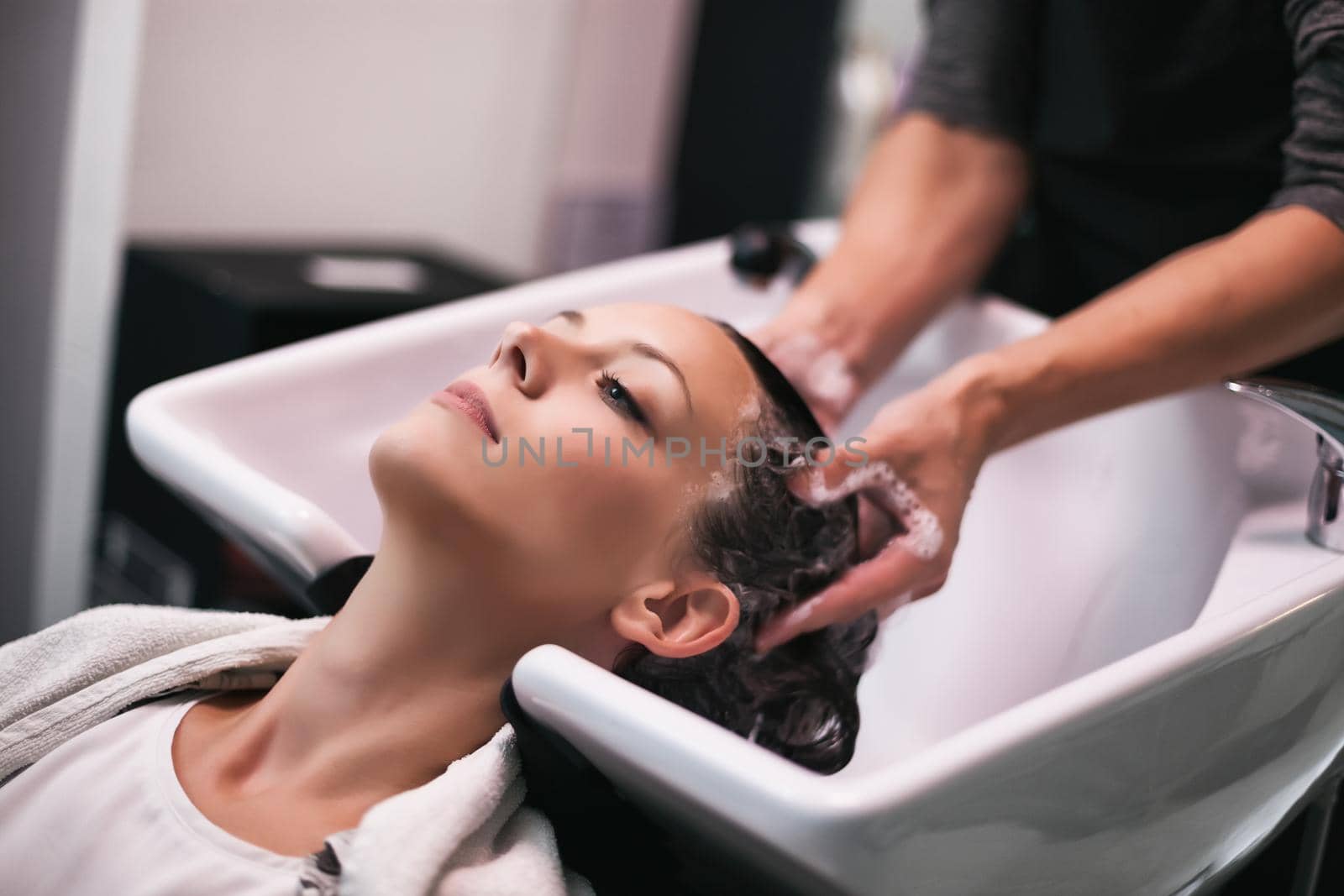 Young woman getting new hairstyle at professional hair styling saloon. Hairdresser is washing and massaging her head.