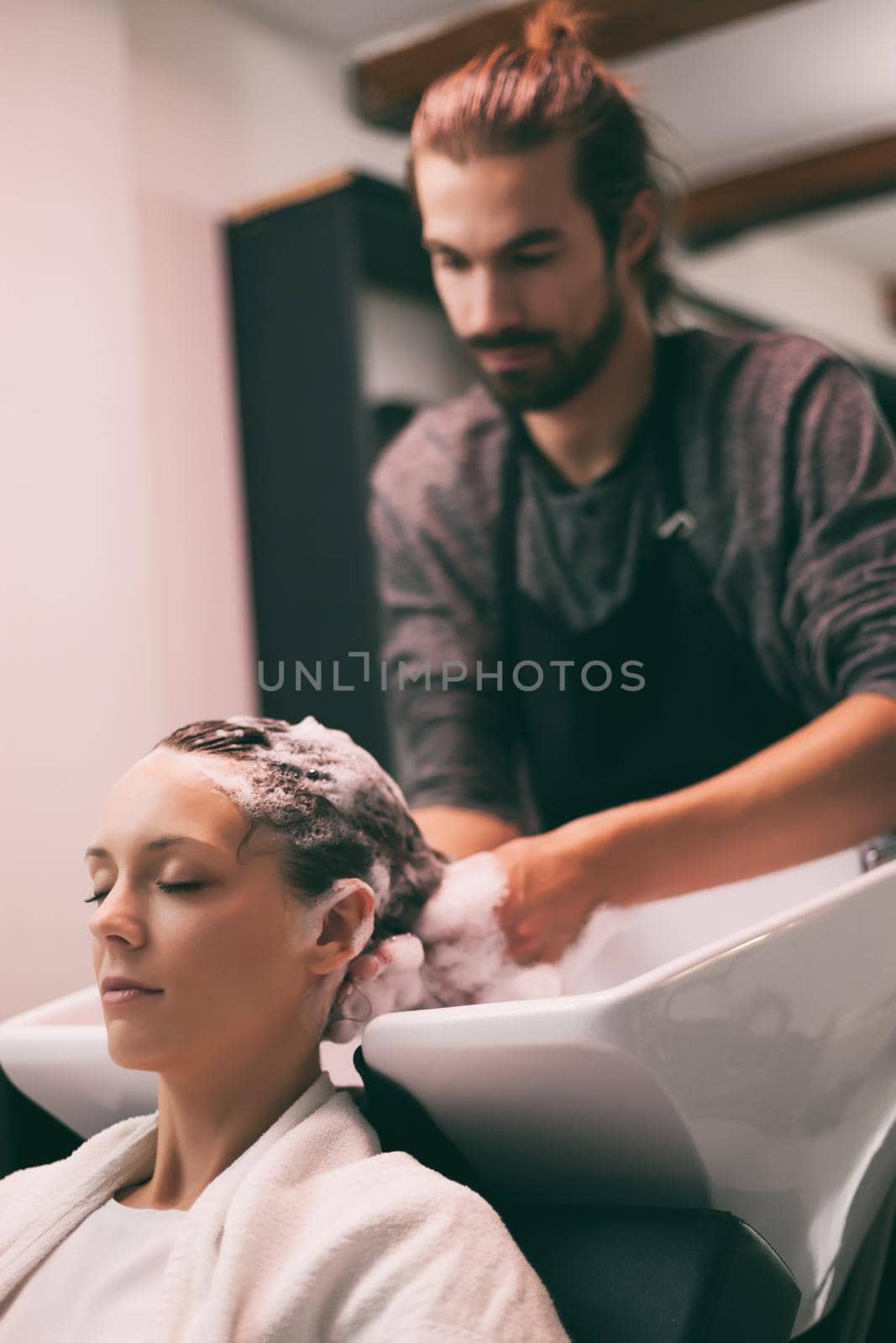 Young woman getting new hairstyle at professional hair styling saloon. Hairdresser is washing and massaging her head.