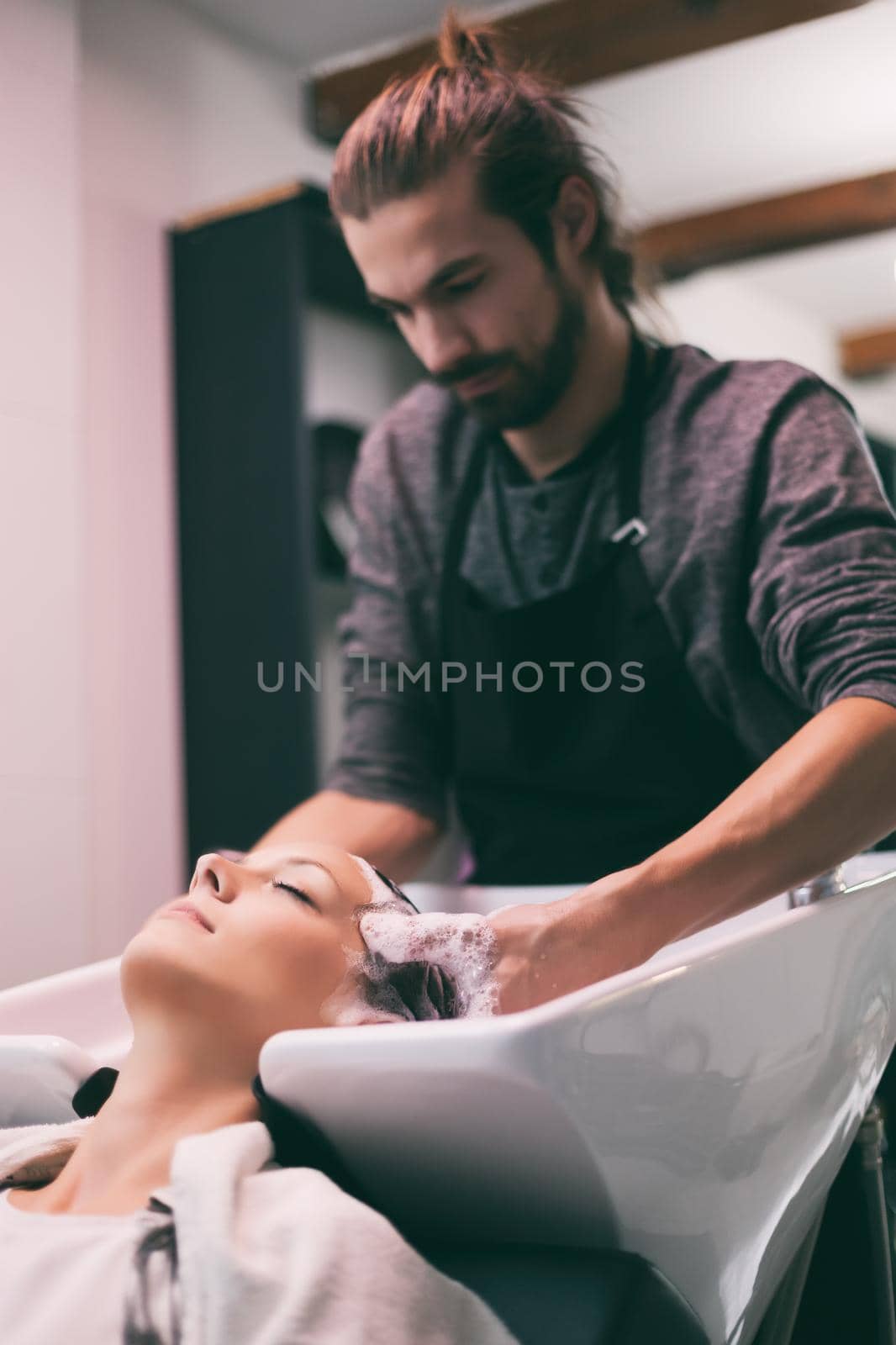 Young woman getting new hairstyle at professional hair styling saloon. Hairdresser is washing and massaging her head.