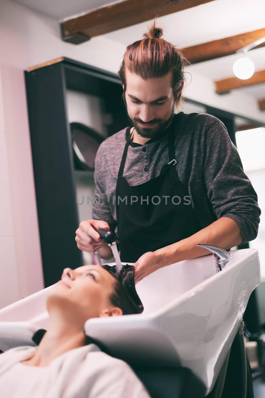 Young woman getting new hairstyle at professional hair styling saloon. Hairdresser is washing and massaging her head.