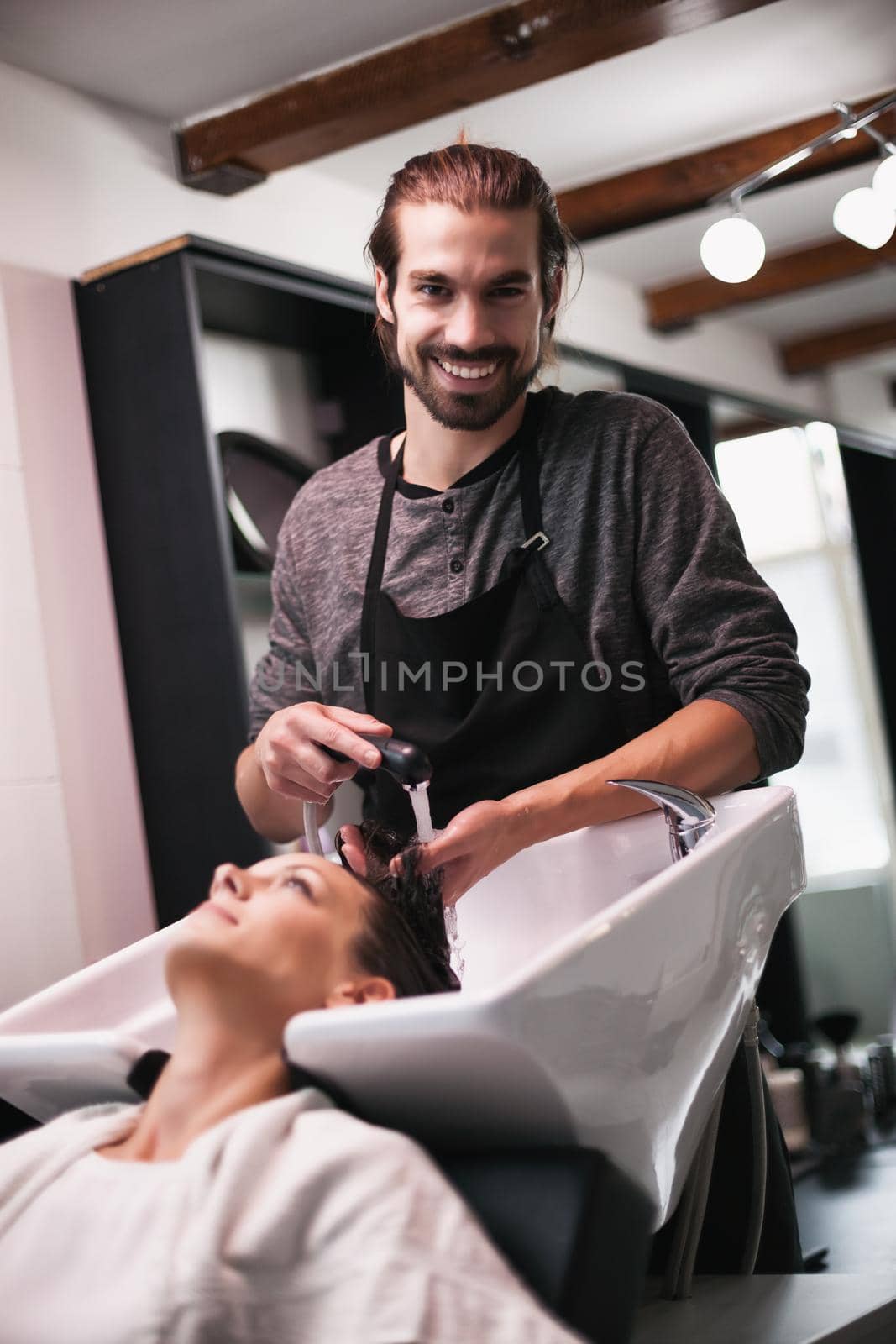 Young woman getting new hairstyle at professional hair styling saloon. Hairdresser is washing and massaging her head.