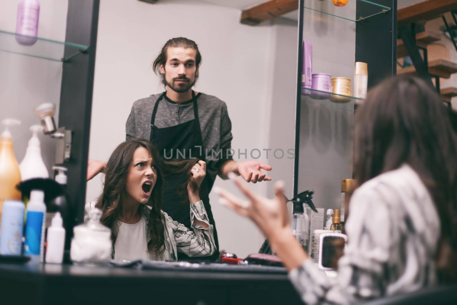 Young woman getting new hairstyle at professional hair styling saloon. She is not satisfied with her new hairstyle.