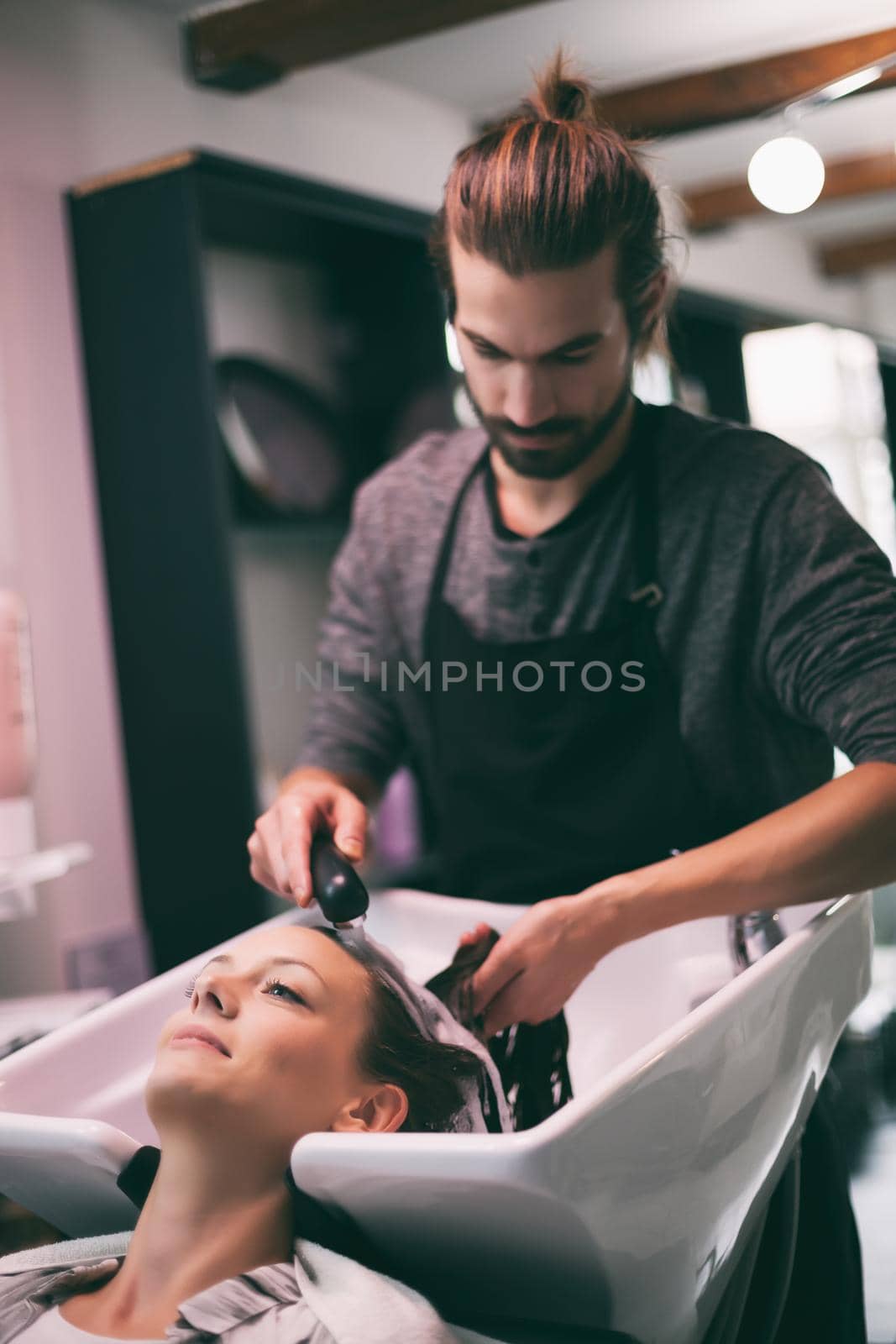 Young woman getting new hairstyle at professional hair styling saloon. Hairdresser is washing and massaging her head.