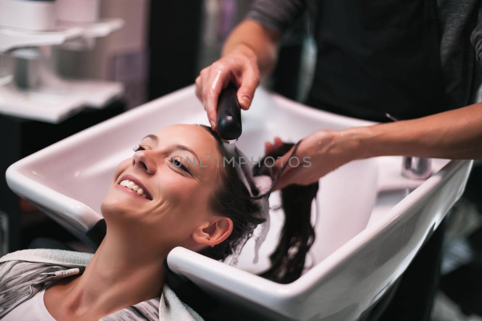 Young woman getting new hairstyle at professional hair styling saloon. Hairdresser is washing and massaging her head.