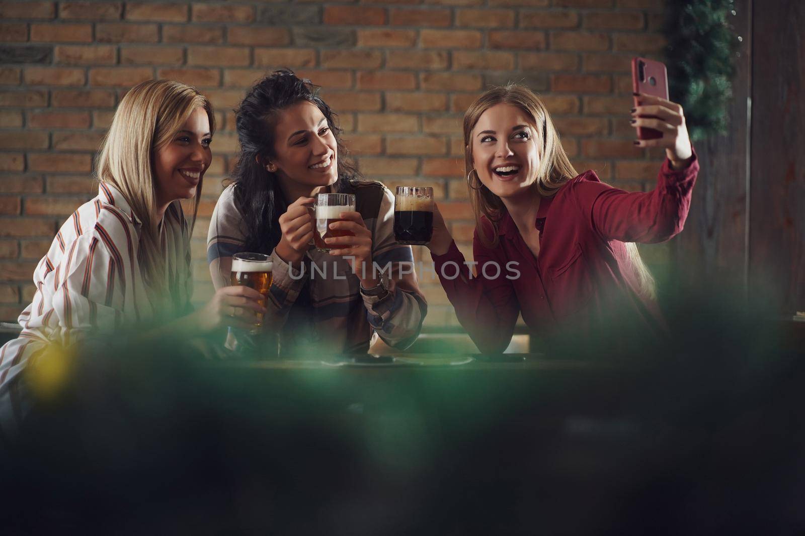 Three happy girlfriends are having fun time in pub. They are talking and drinking beer. Friendship concept.