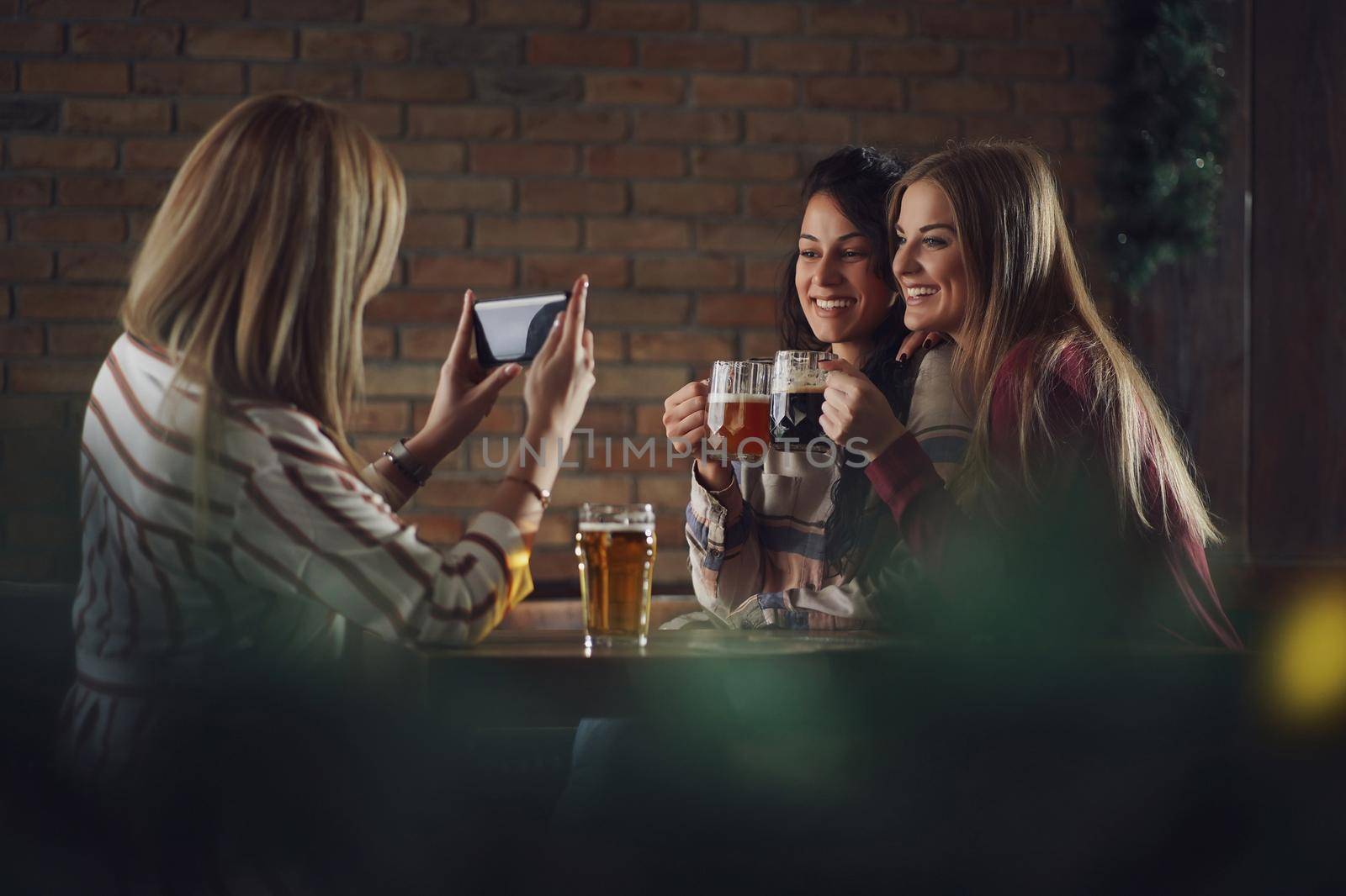 Three happy girlfriends are having fun time in pub. They are talking and drinking beer. Friendship concept.