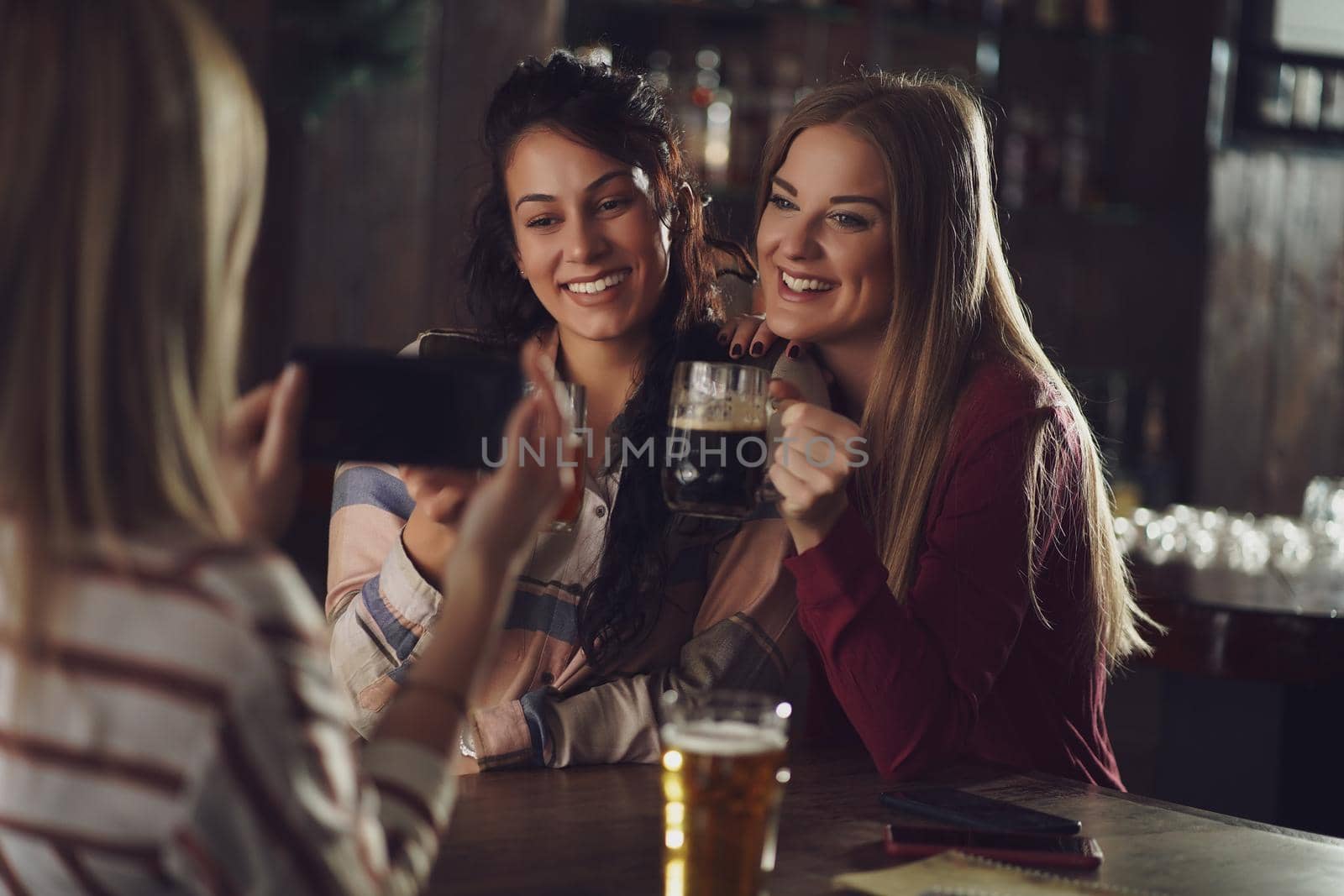 Three happy girlfriends are having fun time in pub. They are talking and drinking beer. Friendship concept.