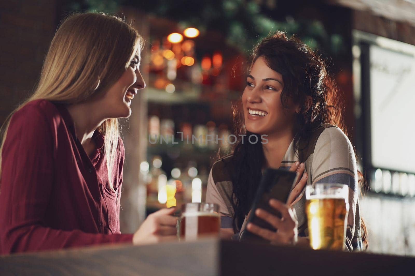 Two happy girlfriends are having fun time in pub. They are talking. Friendship concept.
