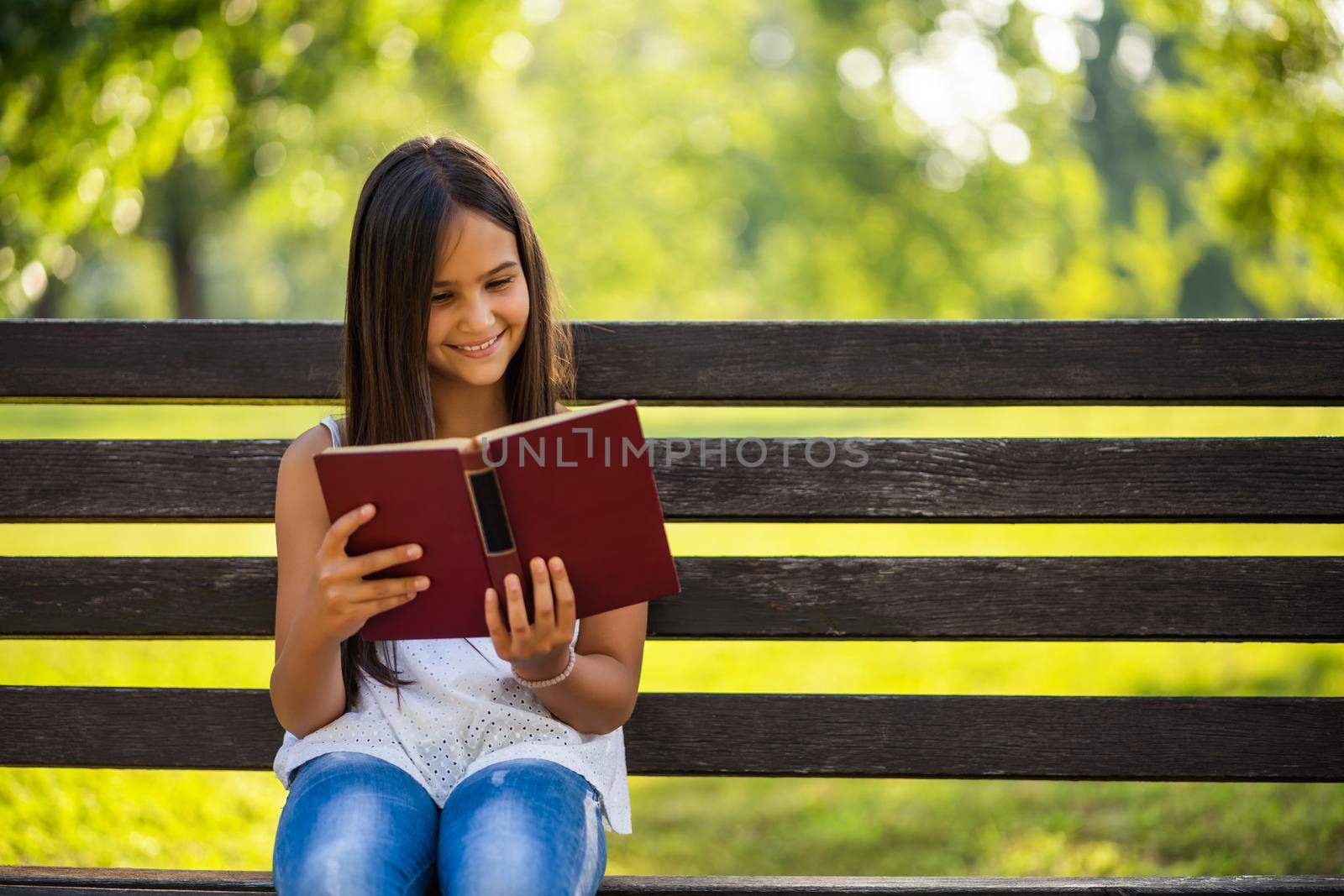 Happy little girl is reading a book in park.