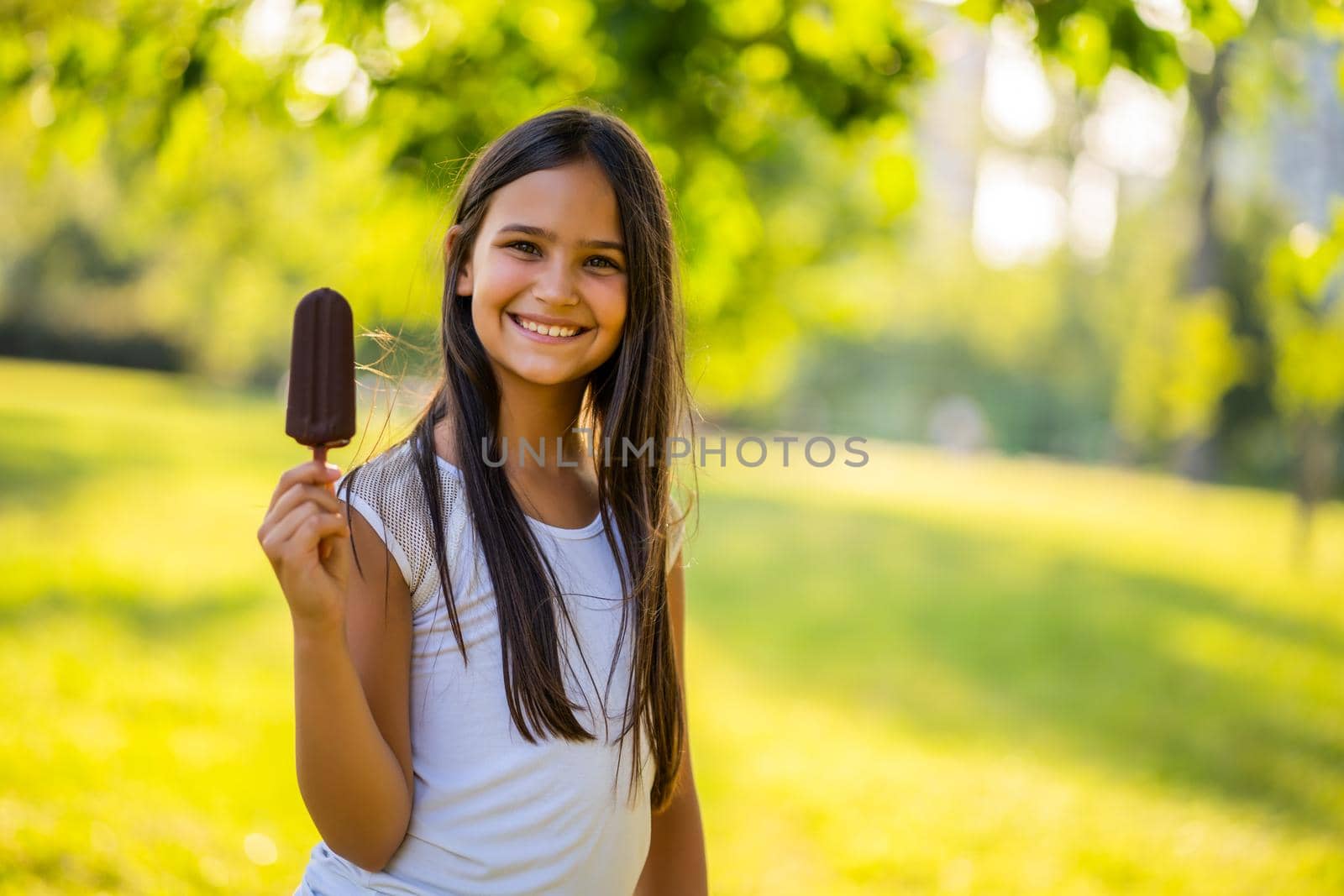 Happy little girl is eating ice cream in park.