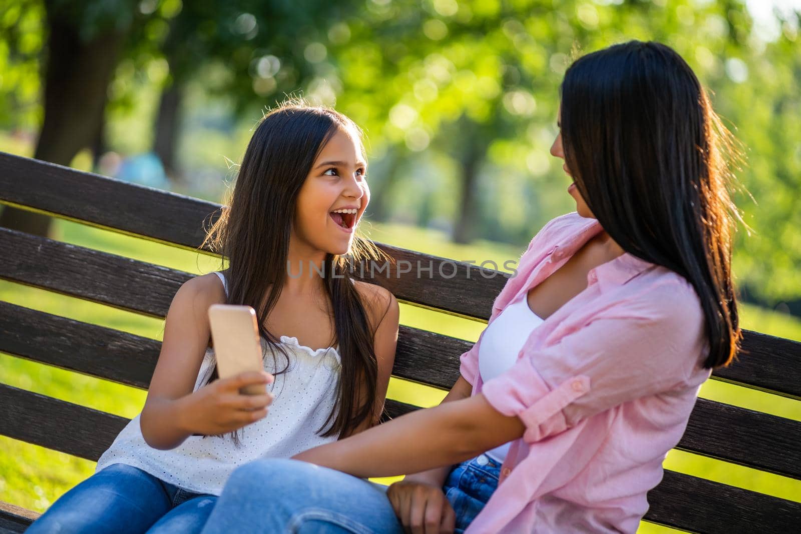 Happy family having nice time in park together. They are using smartphone.