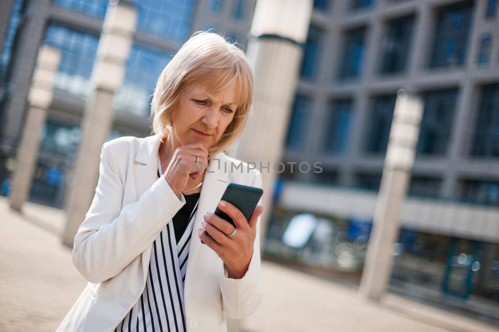 Outdoor portrait of worried senior businesswoman who is using smartphone.